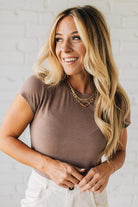 Woman wearing a brown top and white pants against a white brick wall