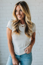 Woman wearing a white t-shirt and blue jeans against a white brick wall.