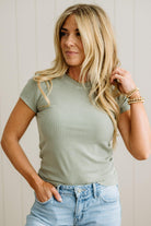 Woman wearing a green t-shirt and blue jeans against a plain background