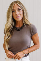 Woman wearing a brown t-shirt and brown jeans against a neutral background