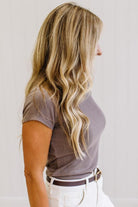 Woman wearing a brown t-shirt and white jeans against a neutral background