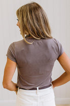 Woman wearing a brown t-shirt and white jeans against a neutral background