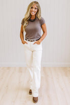 Woman wearing a brown t-shirt and white jeans against a neutral background