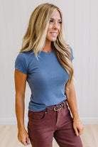 Woman wearing a blue t-shirt and brown jeans against a neutral background