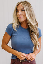 Woman wearing a blue t-shirt and brown jeans against a neutral background
