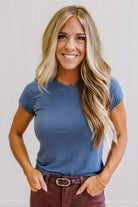 Woman wearing a blue t-shirt and brown jeans against a neutral background