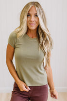 Woman wearing a green t-shirt and brown jeans against a neutral background
