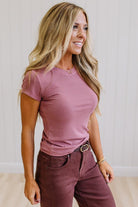 Woman wearing a pink t-shirt and brown jeans against a neutral background