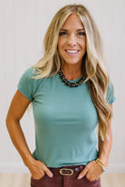 Woman wearing a teal t-shirt and brown jeans against a neutral background