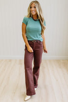Woman wearing a teal t-shirt and brown jeans against a neutral background