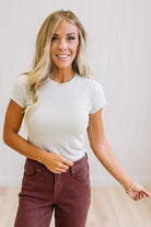 Woman wearing a cream t-shirt and brown jeans against a neutral background