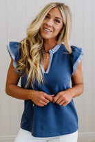 Woman wearing a blue top with ruffled shoulders against a neutral background