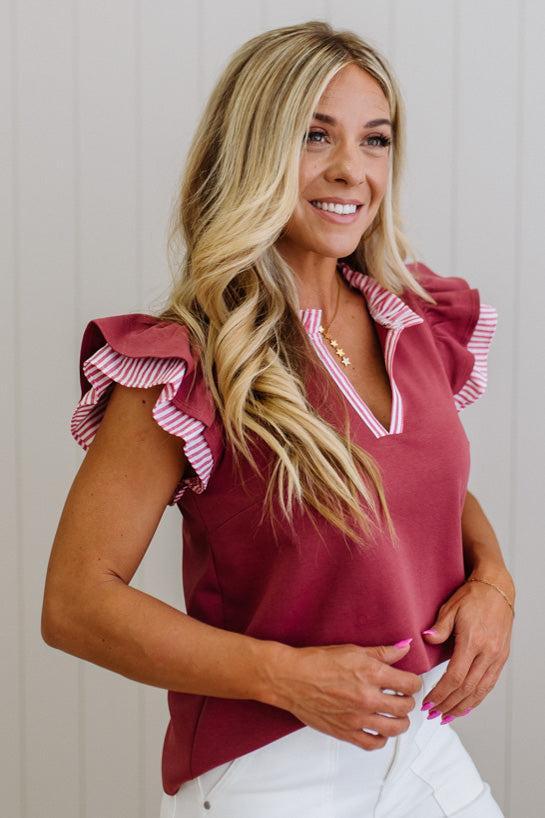 Woman wearing a burgundy top with ruffled sleeves against a neutral background