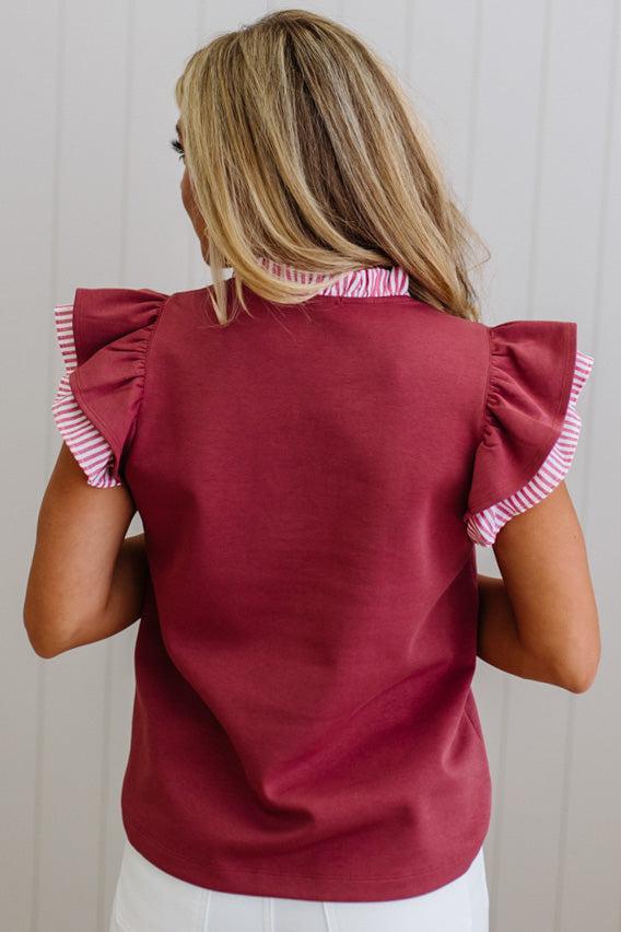 Woman wearing a burgundy top with ruffled sleeves against a neutral background