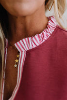 Close-up of a person wearing a red top with a striped neckline and gold star-shaped earrings.