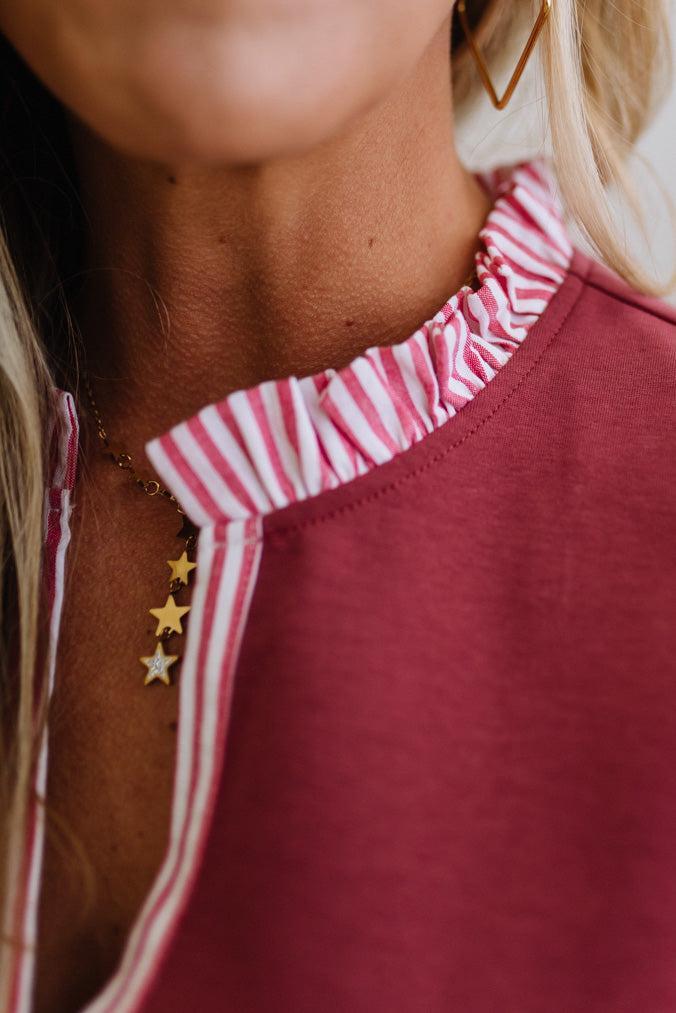 Close-up of a person wearing a red top with a striped neckline and gold star-shaped earrings.