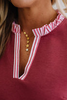 Close-up of a person wearing a red top with white trim and gold star necklaces.