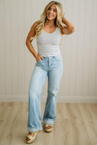 Woman wearing a striped tank top and light blue jeans standing against a neutral wall.
