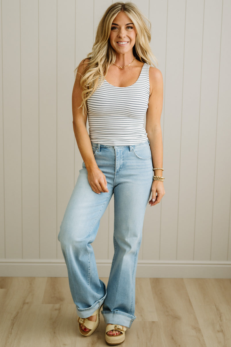Woman wearing a striped tank top and light blue jeans against a neutral background
