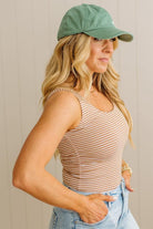 Woman wearing a striped tank top and green cap against a neutral background