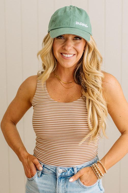 Woman wearing a green cap and striped tank top with a neutral background
