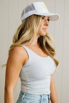 Woman wearing a white tank top and a white cap with a yellow logo against a neutral background