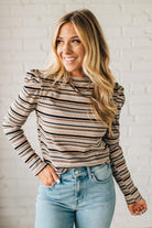 Woman wearing a striped long-sleeve top and jeans against a white brick wall.