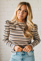 Woman wearing a striped long-sleeve top and jeans against a white brick wall.