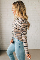 Woman wearing a striped long-sleeve top and light blue jeans against a white brick wall.