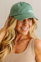 Woman wearing a green cap with 'MOM' printed on it, smiling against a neutral background.
