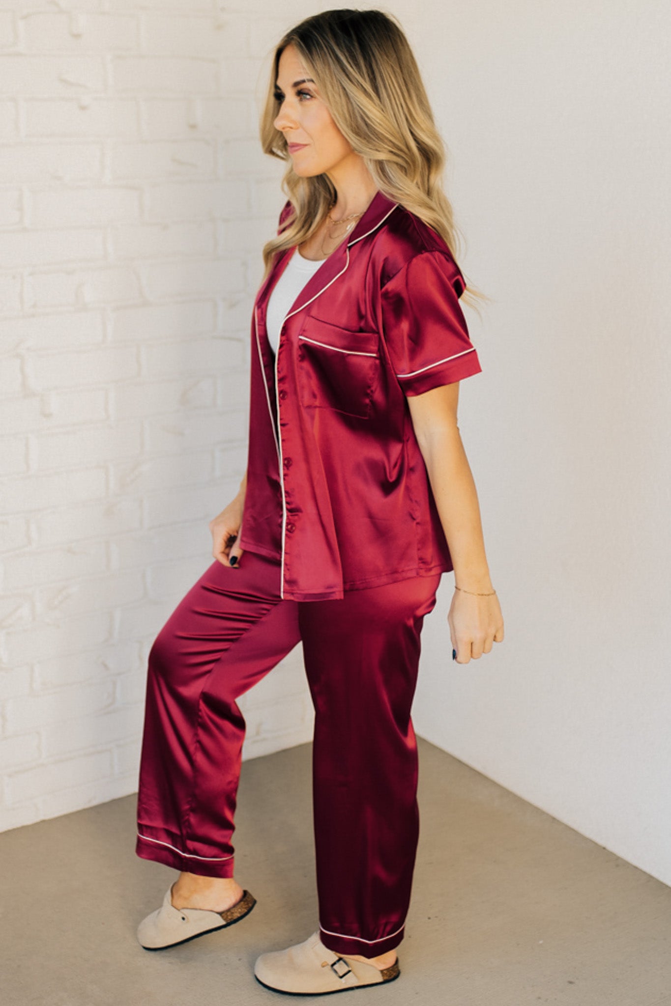 Blonde woman wearing a silk pajama set with white piping. 