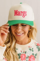 Woman wearing a cap with 'Margs' on it, smiling against a plain background