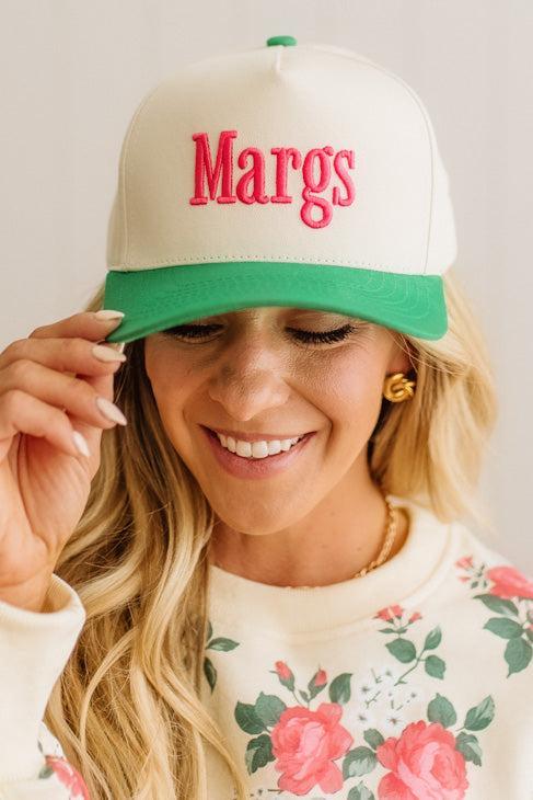 Woman wearing a cap with 'Margs' on it, smiling against a plain background