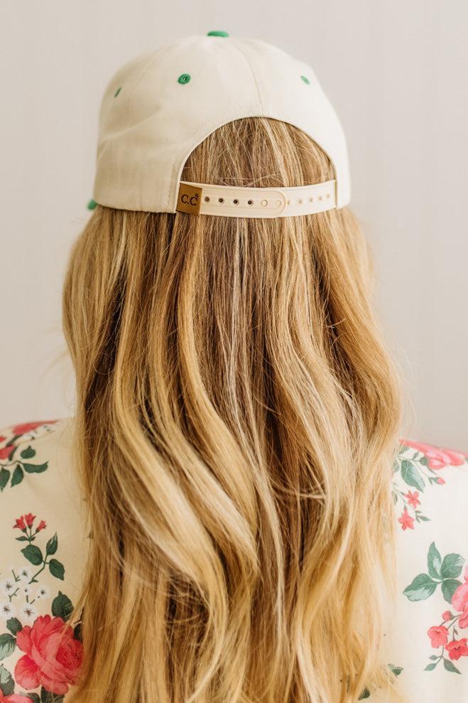 Person wearing a beige cap with green accents and a white band, sitting on a floral chair.