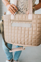 Woman holding a mocha nylon quilted traveler tote bag.