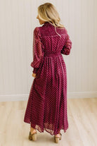 Blonde woman in a brightly lit studio wearing boots and a long dark red dress with full button front and pintucked bodice.