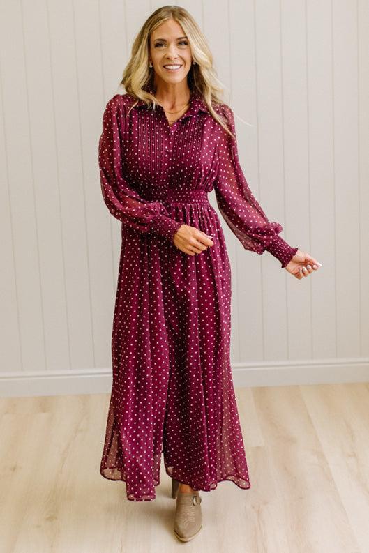 Blonde woman in a brightly lit studio wearing boots and a long dark red dress with full button front and pintucked bodice.