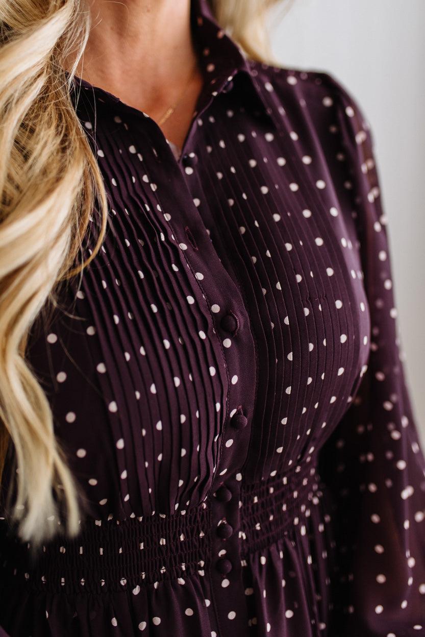 Blonde woman in a brightly lit studio wearing boots and a long dark purpleish brown dress with full button front and pintucked bodice.