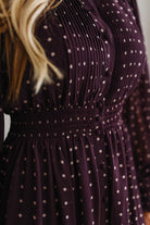 Blonde woman in a brightly lit studio wearing boots and a long dark purpleish brown dress with full button front and pintucked bodice.
