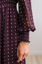 Blonde woman in a brightly lit studio wearing boots and a long dark purpleish brown dress with full button front and pintucked bodice.
