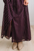 Blonde woman in a brightly lit studio wearing boots and a long dark purpleish brown dress with full button front and pintucked bodice.