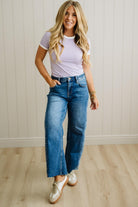 Woman wearing a striped shirt and blue jeans standing against a light wooden paneled wall.