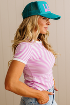 Woman wearing a pink striped shirt and teal cap with pink logo against a beige background