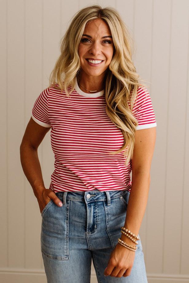 Woman wearing a red and white striped shirt and blue jeans against a beige wall.