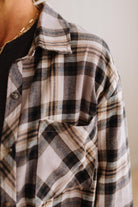 Close-up of a person wearing an oversized plaid button-up shirt in beige, black, and gray tones over a black top, with a gold chain necklace visible.