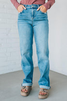 Person wearing blue jeans and a pink top against a white brick wall.