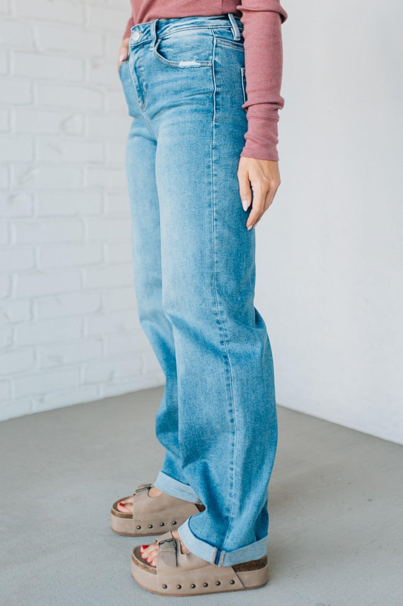 Person wearing blue jeans and a pink top against a white brick wall.