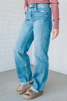 Person wearing light blue jeans and a pink top against a white brick wall.