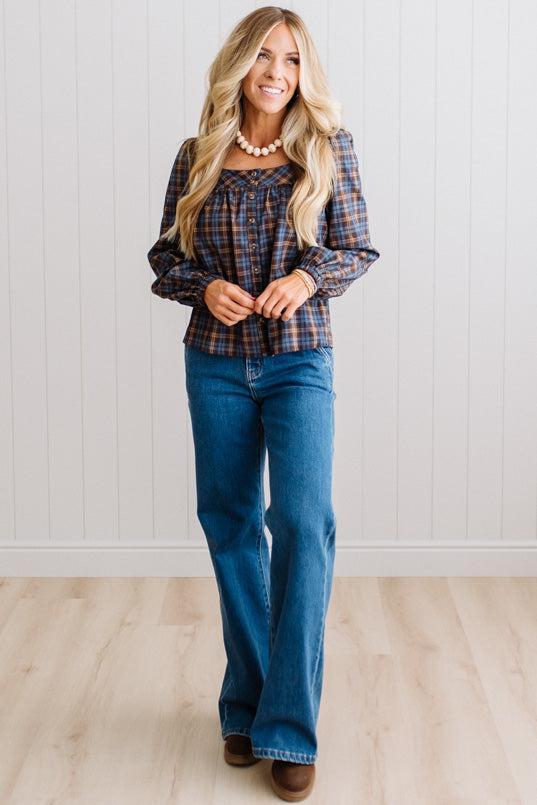 Blonde woman in a brightly lit studio wearing a PLAID SQUARE NECK BUTTON CLOSURE FRONT LONG SLEEVE BLOUSE  WITH DARK JEANS AND BROWN BOOTS.