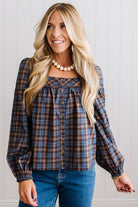 Blonde woman in a brightly lit studio wearing a PLAID SQUARE NECK BUTTON CLOSURE FRONT LONG SLEEVE BLOUSE  WITH DARK JEANS AND BROWN BOOTS.